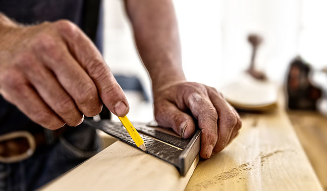 carpenter measures on piece of wood marks with pencil