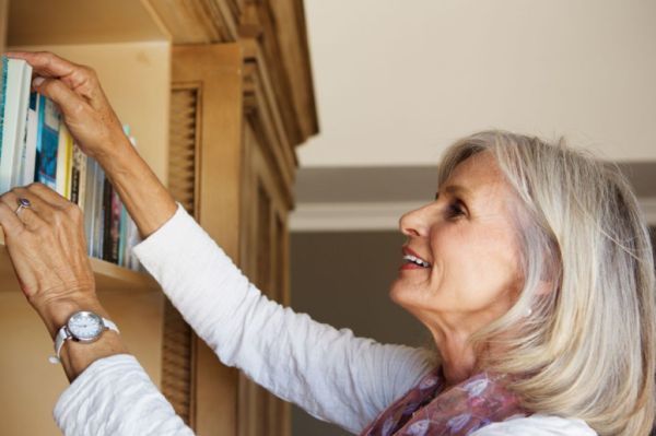 Frozen shoulder Senior woman reaching to high shelf of bookcase