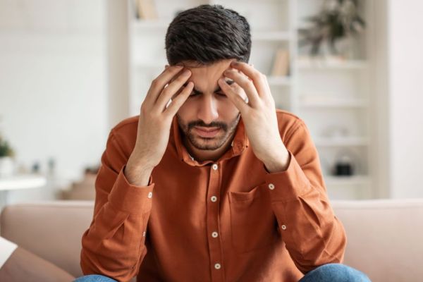 Man sitting on couch with his head in his hands, experiencing a headache