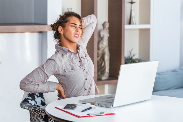 young woman sitting at home office desk in front of laptop, touching aching neck