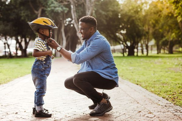 A man helping a child put on a helmet outside