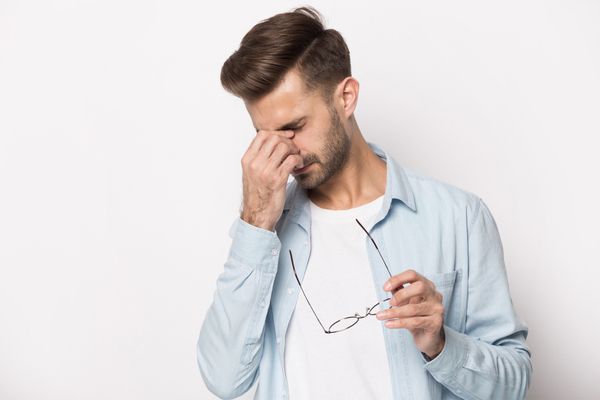 a man taking off his glasses, rubbing his eyes due to dizziness.