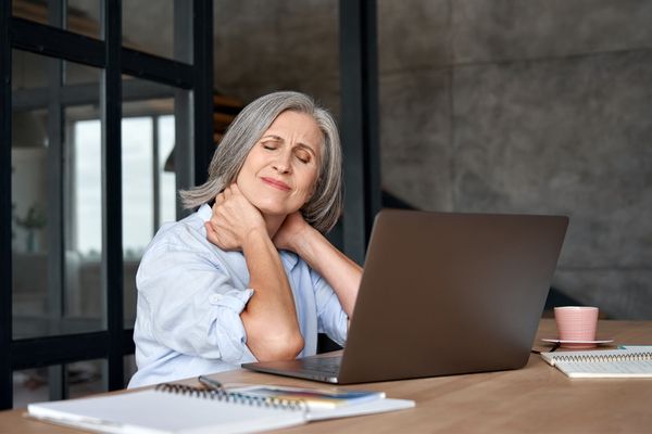 a woman experiencing neck pain sitting at a desk