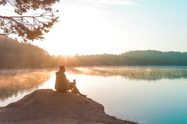 A man sitting alone, meditating and relaxing by a lake.