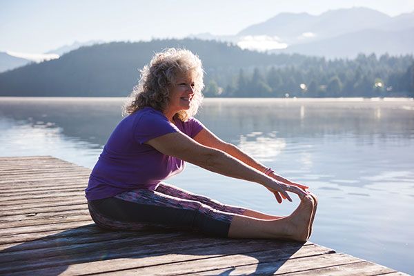 woman stretching her legs on a dock in front of water