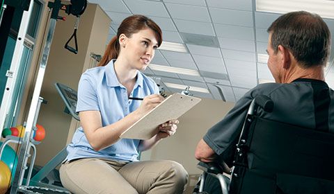 physiotherapist with clipboard talks to man in wheelchair