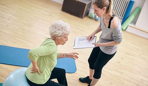 physiotherapist with notebook patient sits on exercise ball