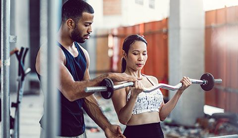 trainer with woman lifting bar weights