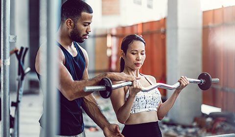 trainer with woman lifting bar weights