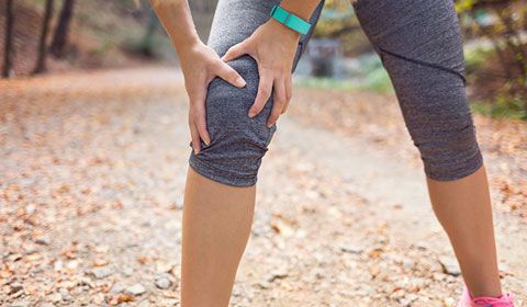 woman outside trail workout clothes holding knee arthritis