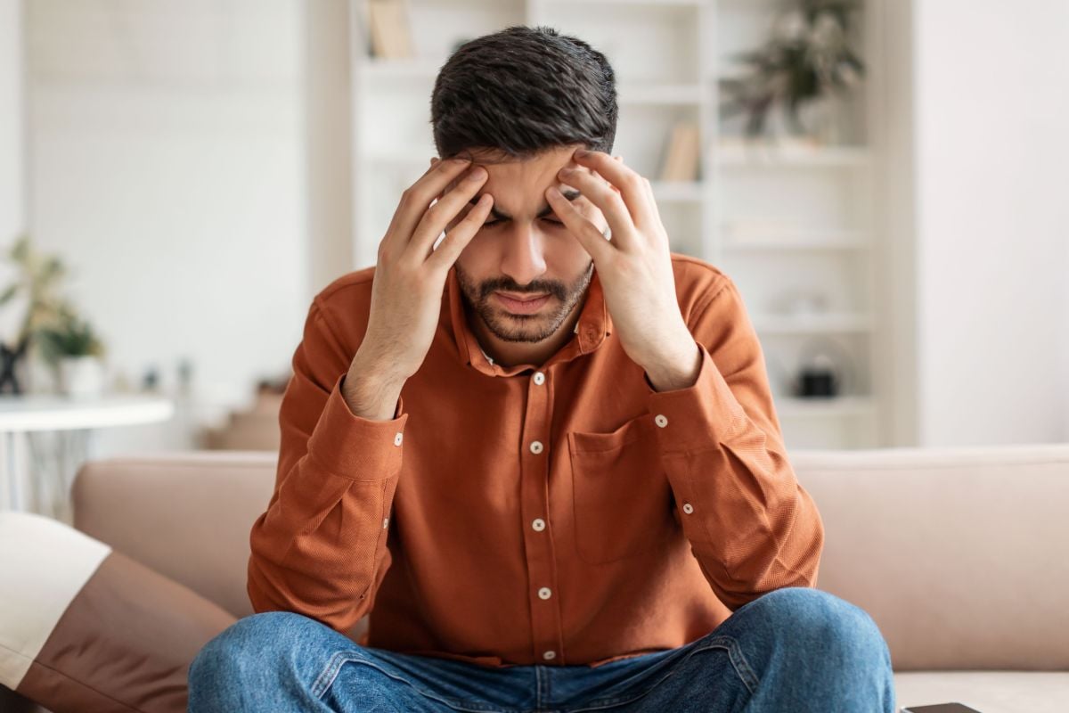 Man sitting on couch with his head in his hands, experiencing a headache