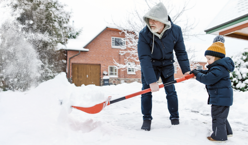 Toddler boy helping his grandfather to shovel snow