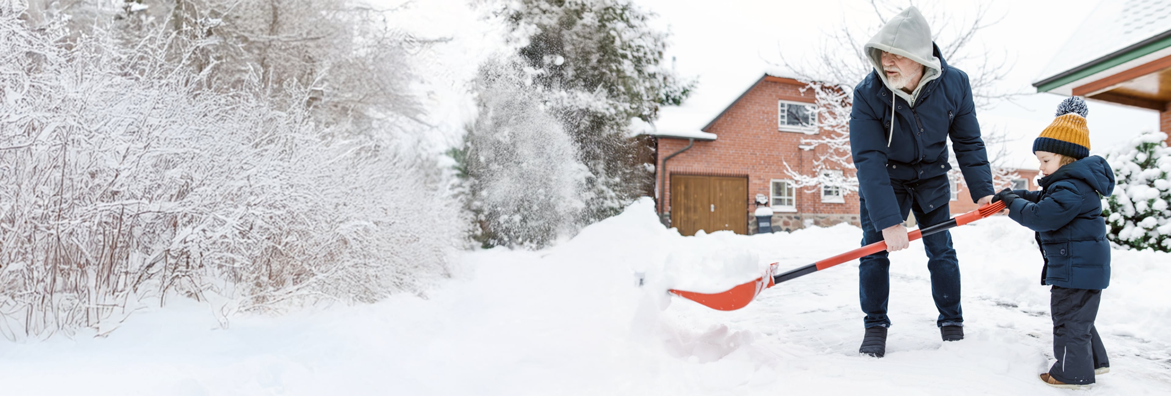 Toddler boy helping his grandfather to shovel snow
