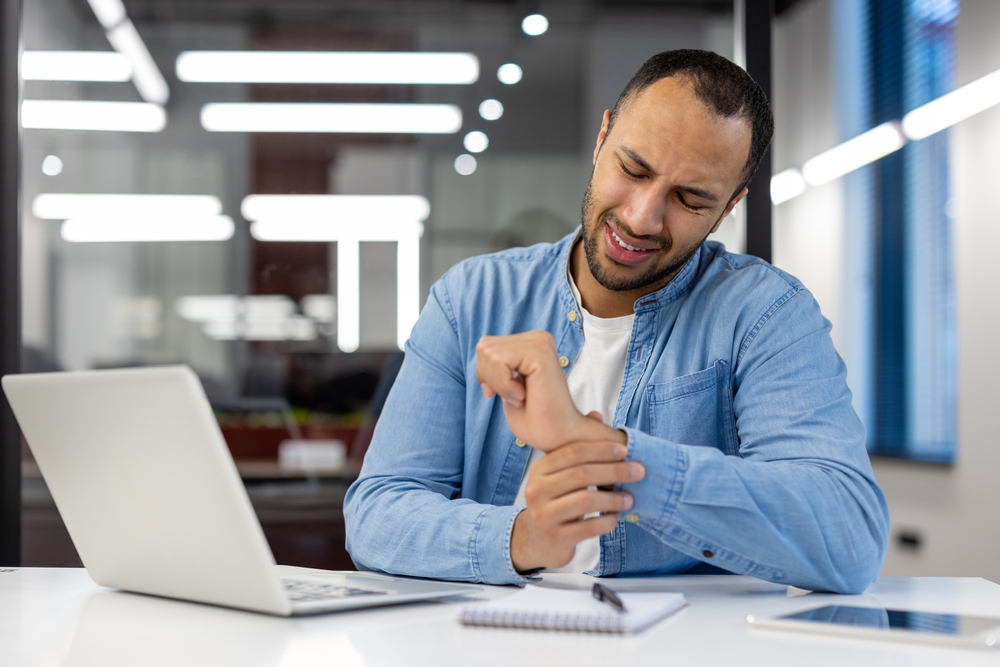 Man with carpal tunnel syndrome sitting at an office desk holding wrist in pain