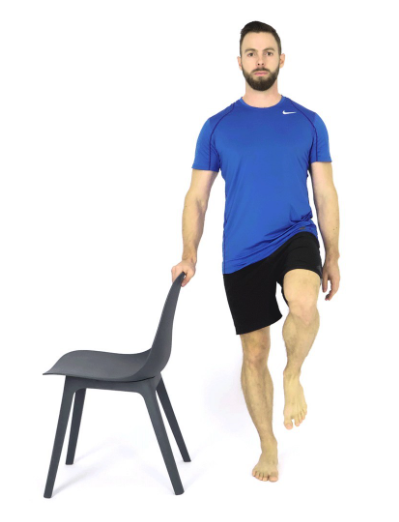 Person balancing on one leg beside a chair