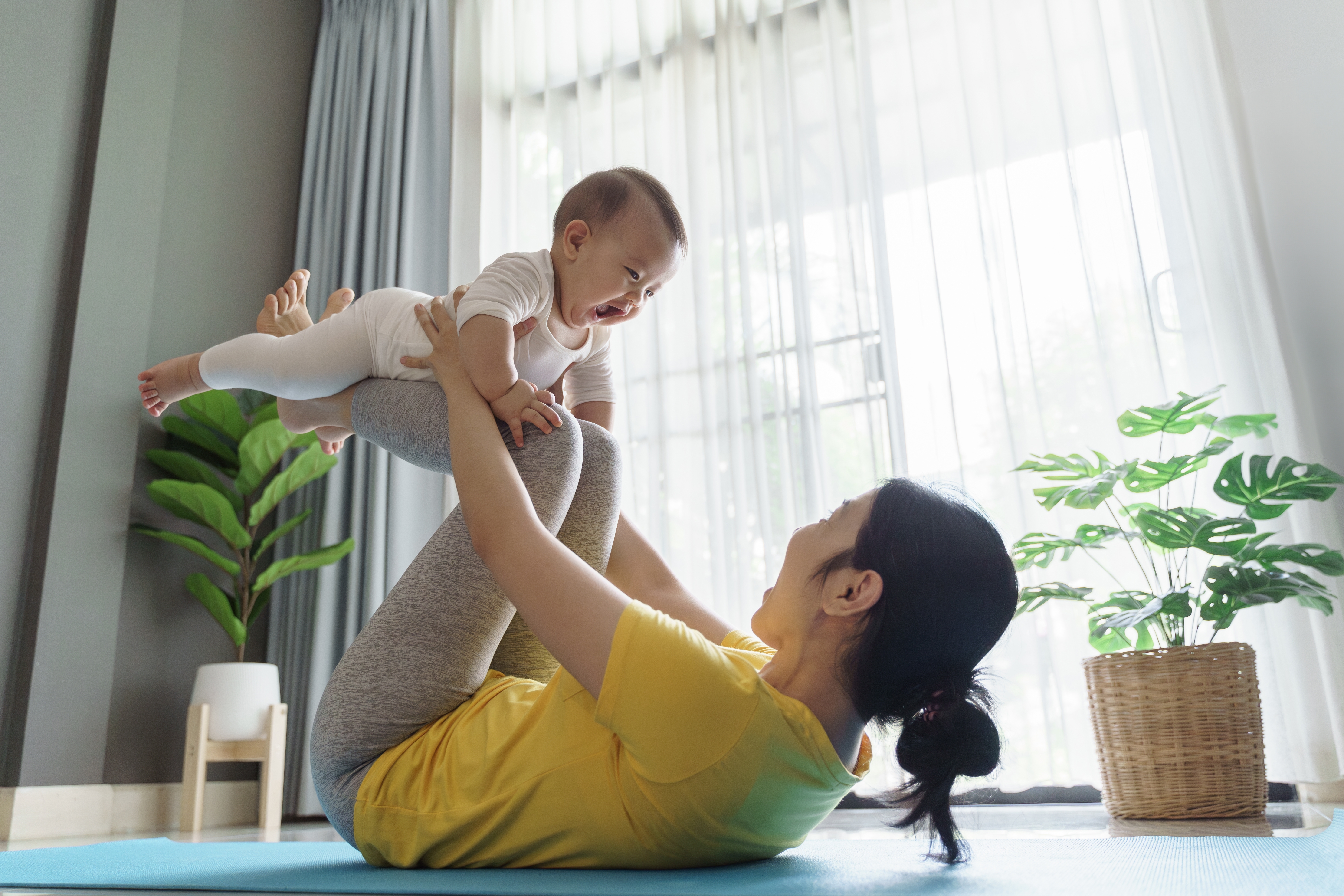 Mother lifting baby while doing core exercises on yoga mat