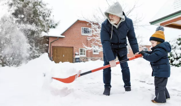 Toddler boy helping his grandfather to shovel snow