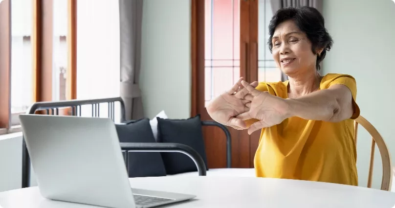 A elderly woman stretching in front of her computer