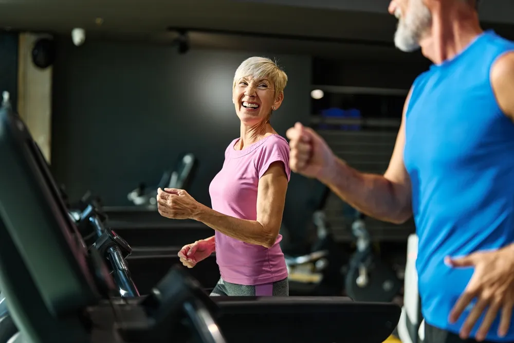 Senior woman and man happily running on treadmill