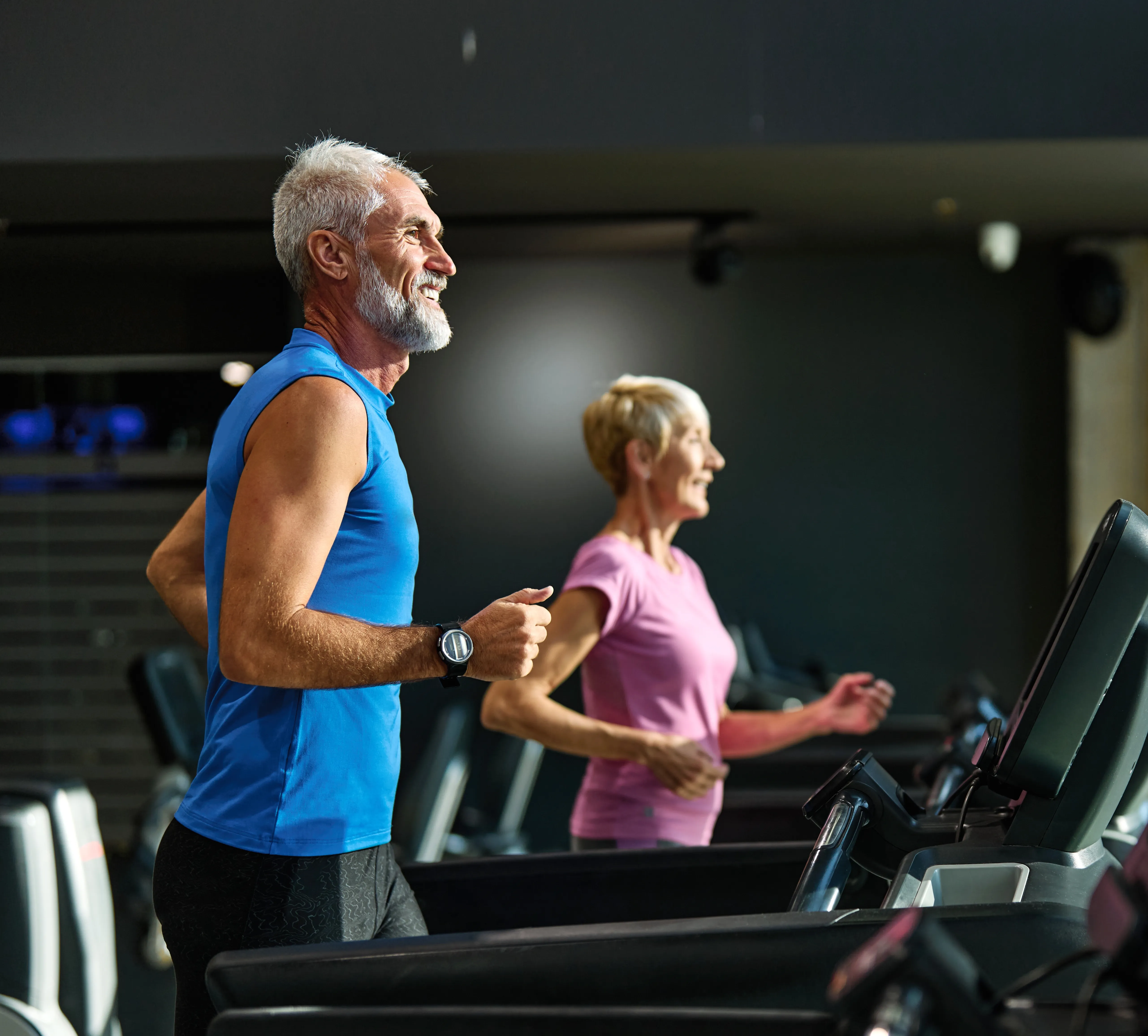 Senior man and woman running indoors on treadmill