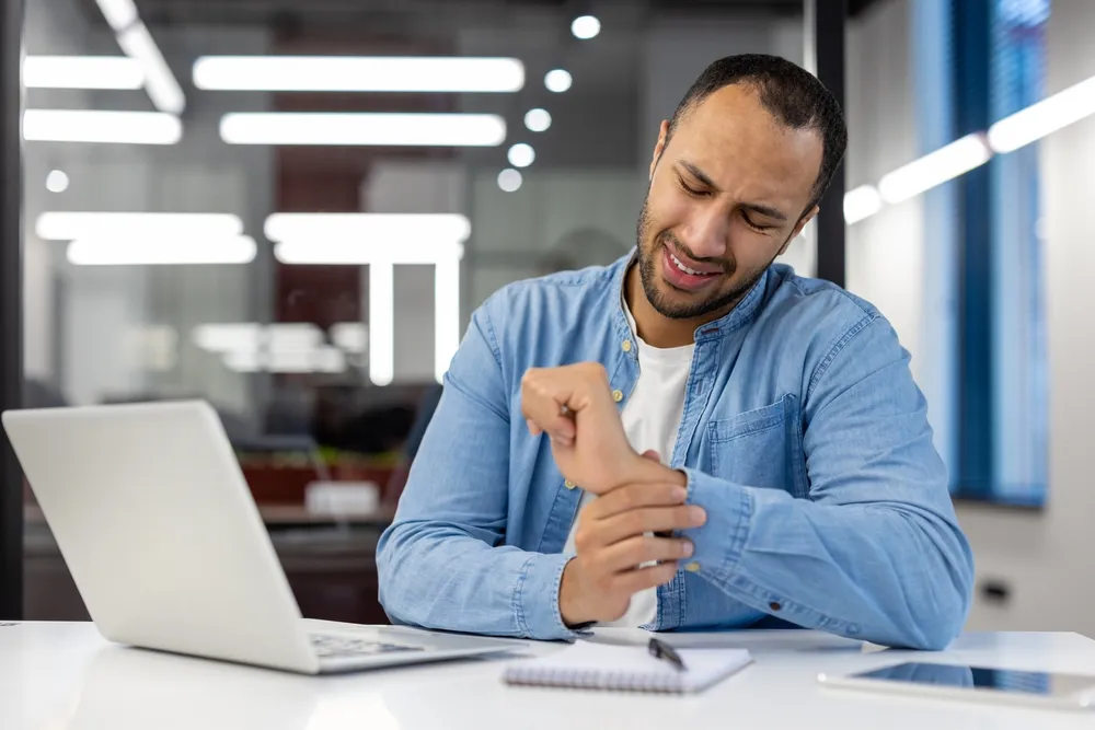 Man with carpal tunnel syndrome sitting at an office desk holding wrist in pain